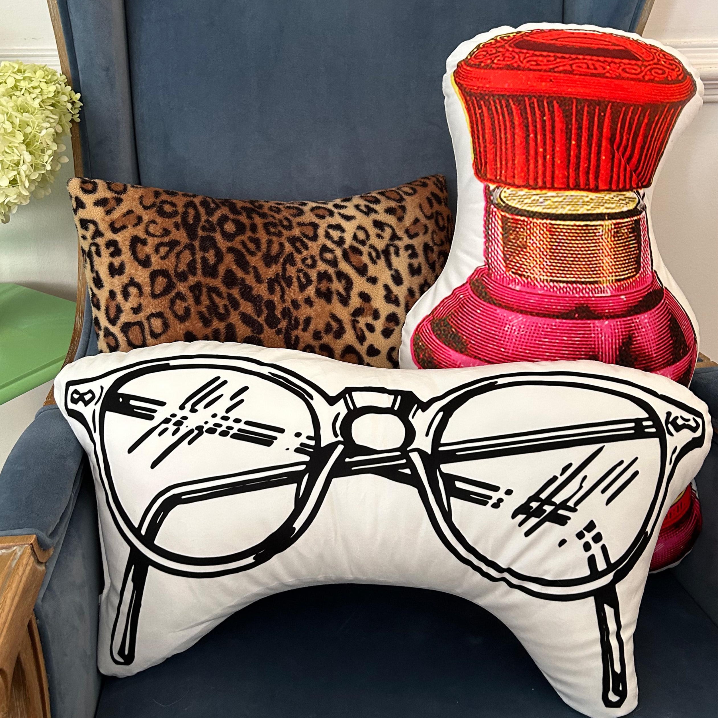 Decorative pillows with leopard print, red perfume bottle, and glasses illustration on a blue chair.
